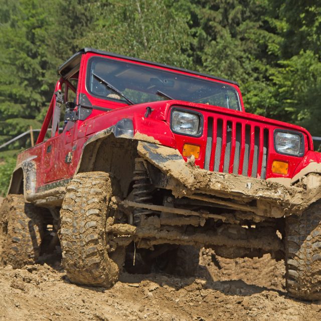 Red off-road vehicle in muddy terrain. All potential trademarks are removed.